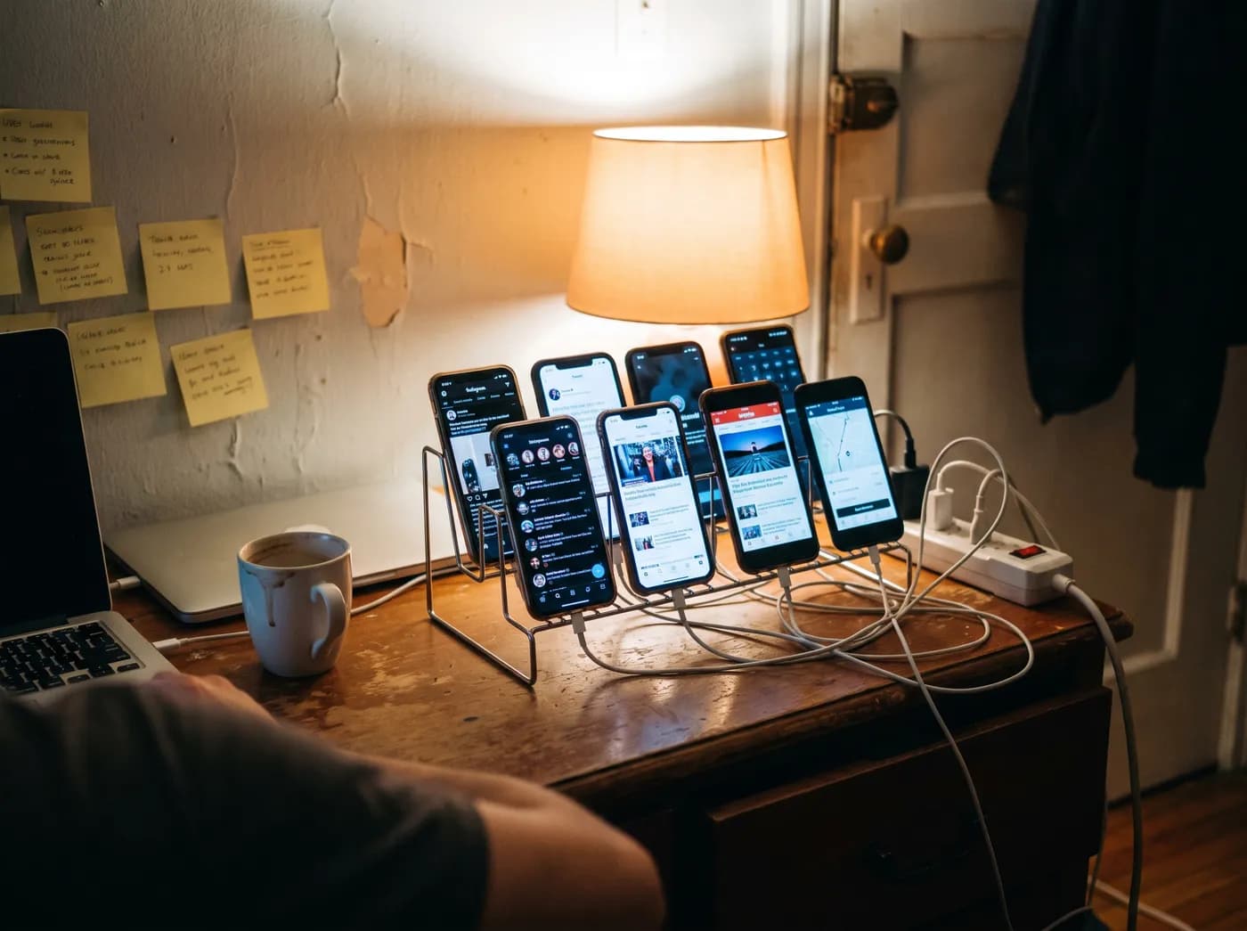 Eight phones on a cheap stand at a VA's desk, tangled in charging cables, next to a laptop and sticky notes
